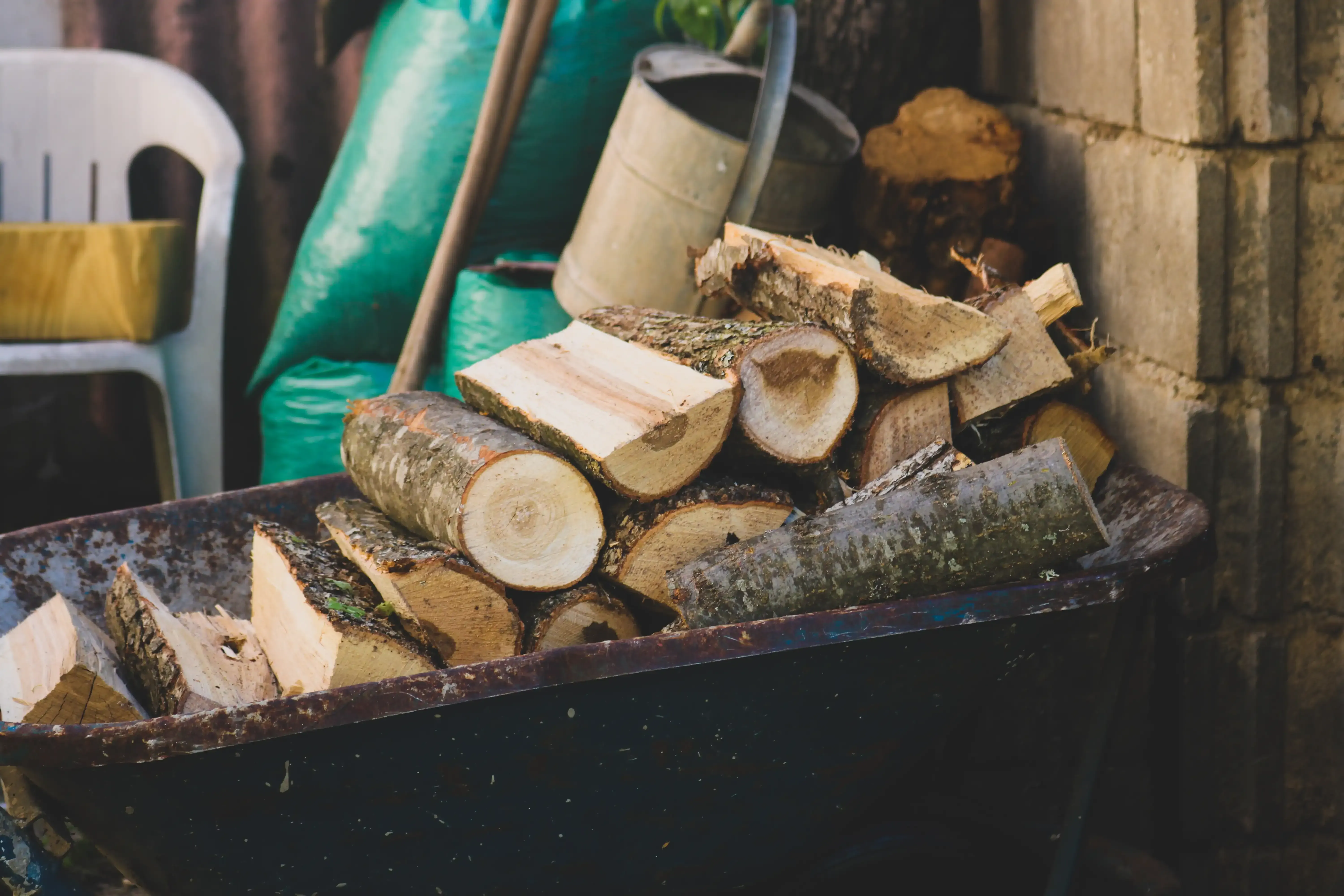 A wheelbarrow filled with logs is sitting in front of a brick wall.